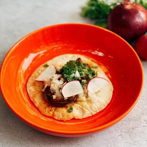 A single Sullivan Taqueria taco in an orange bowl, topped with meat, onions, cilantro, and radishes.
