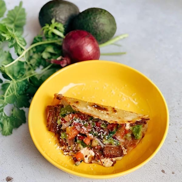 A Sullivan Taqueria quesadilla with meat, salsa, and cheese on a yellow plate, with avocados and onion.