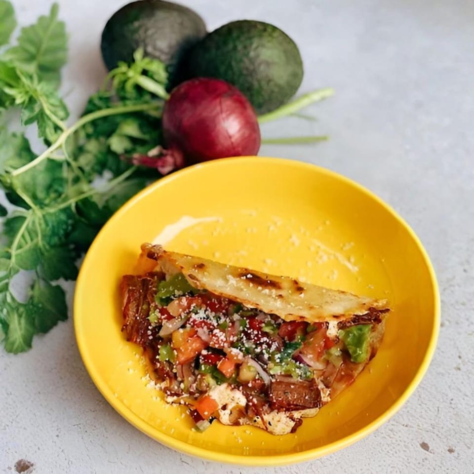 A Sullivan Taqueria quesadilla with meat, salsa, and cheese on a yellow plate, with avocados and onion.