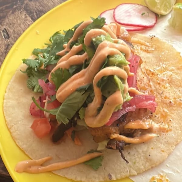 A vibrant Sullivan Taqueria taco on a yellow plate, topped with sauce, cilantro, and pickled onions.