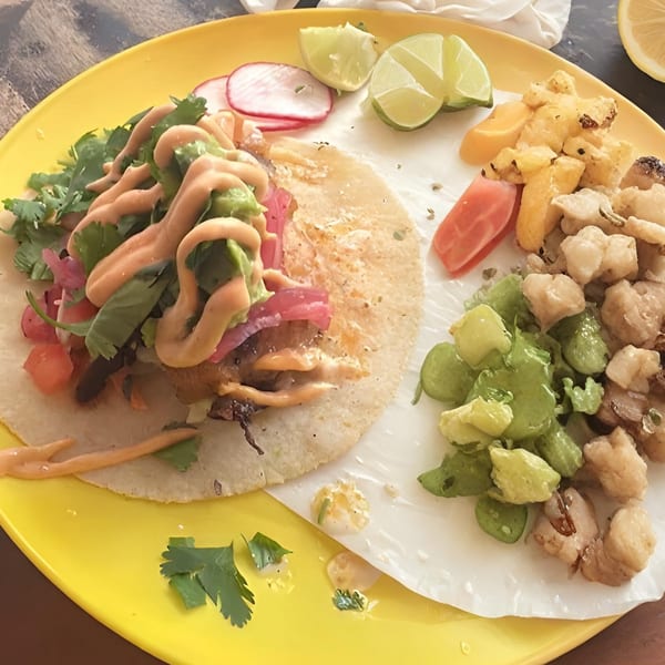 A vibrant taco with sauce, cilantro, and red onions, served with lime, radish, and side dishes.
