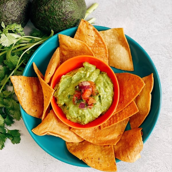 Guacamole with pico de gallo in an orange bowl, surrounded by tortilla chips on a blue plate.