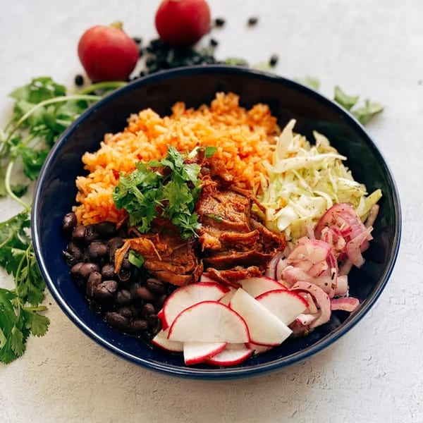 A vibrant Mexican bowl with rice, black beans, shredded meat, cabbage, pickled onions, and radishes.