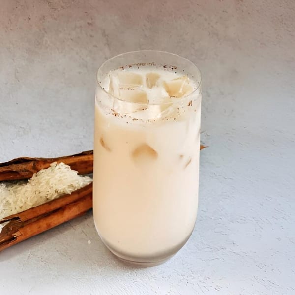 Horchata with ice and cinnamon, next to cinnamon sticks and rice grains.